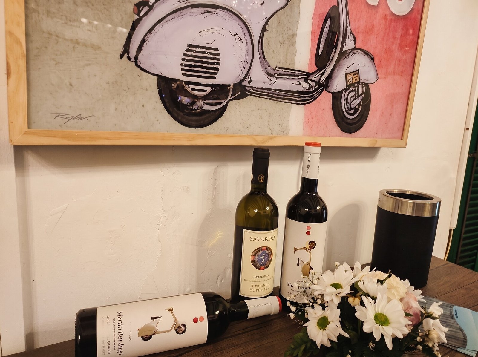 Cuadro de una Vespa y botellas de vino en el interior de La Vespa, Artà